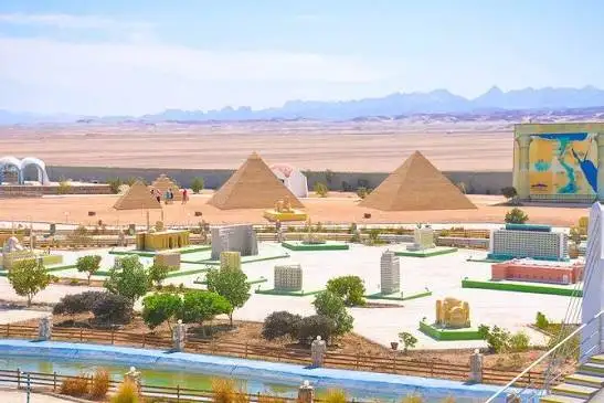 Outdoor miniature park with scale models of the Pyramids of Giza and the Sphinx against a desert and mountain landscape